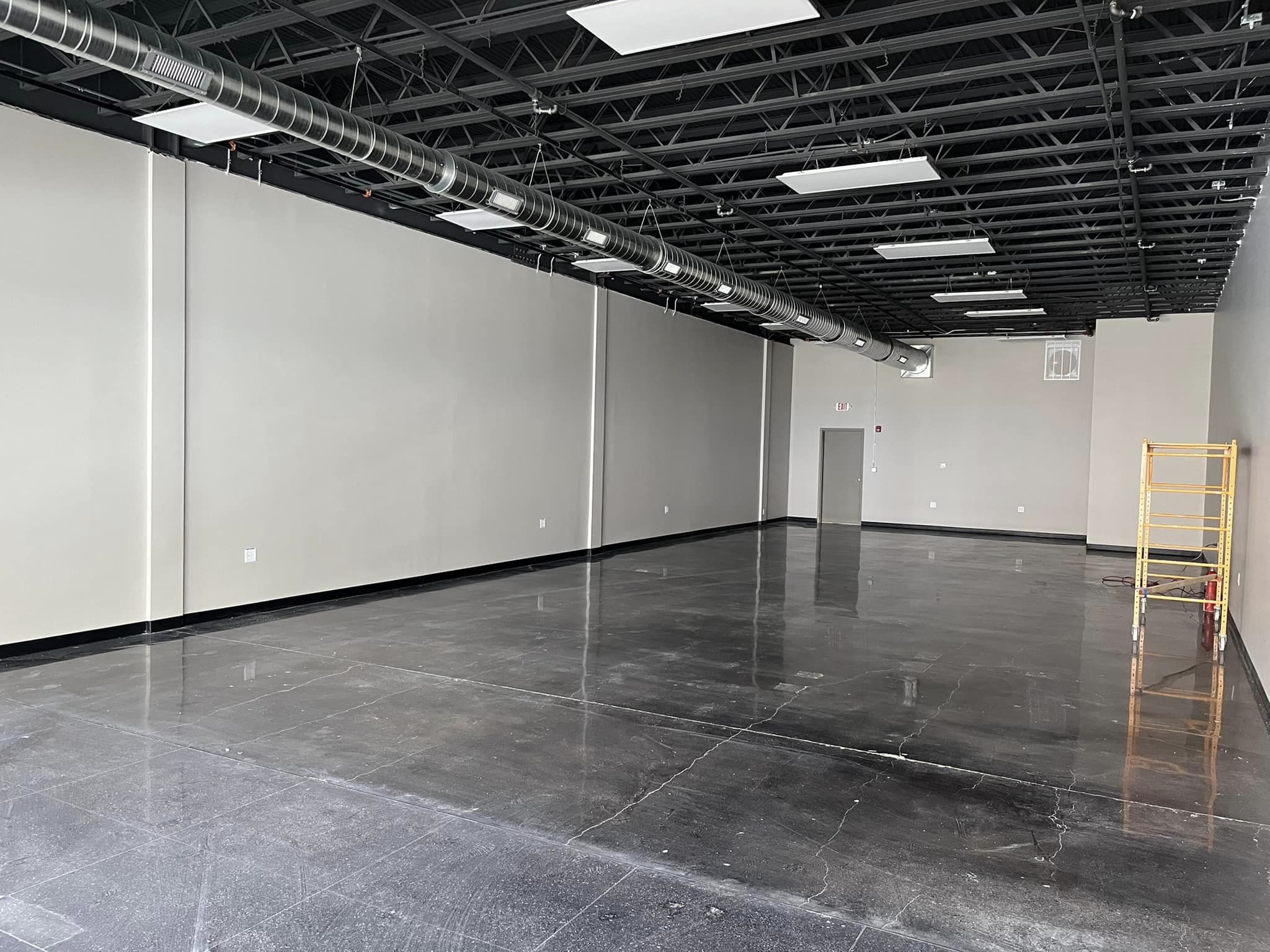Empty space with concrete floors and white walls looking to the back of the space
