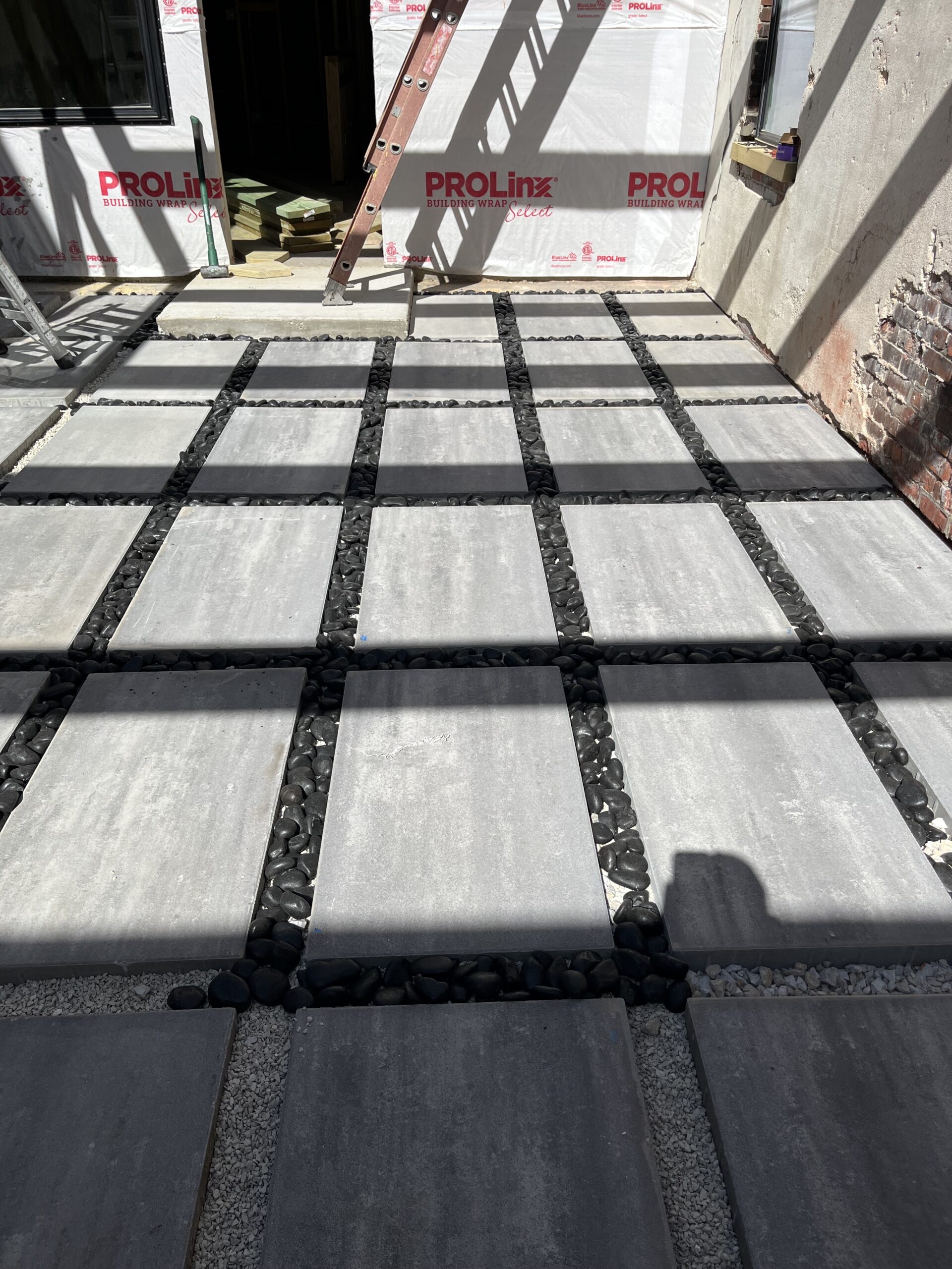 Cement patio of concrete blocks with black gravel in between square slabs