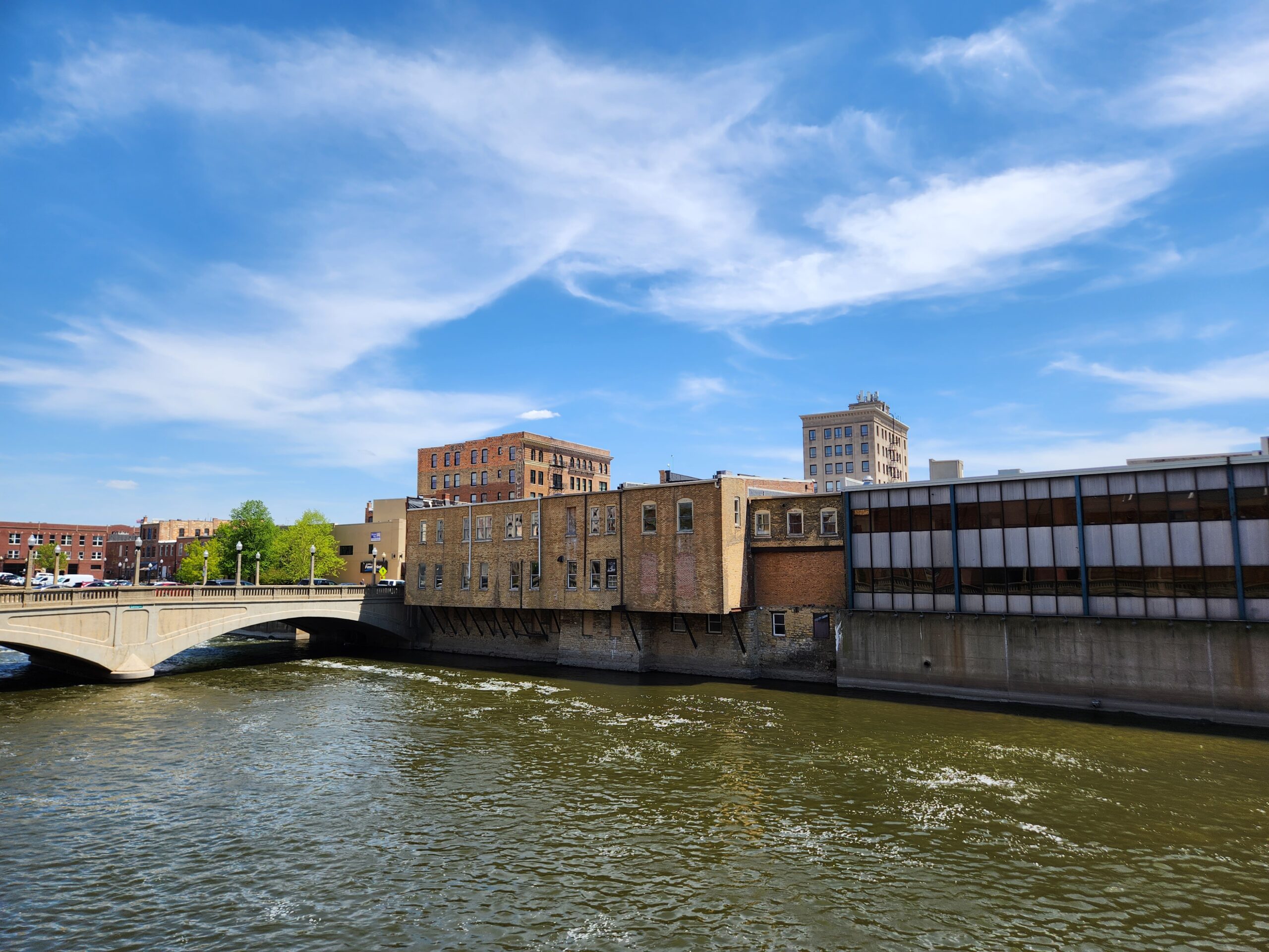 A brick building cantilevered over the Fox River. View is from across the river.
